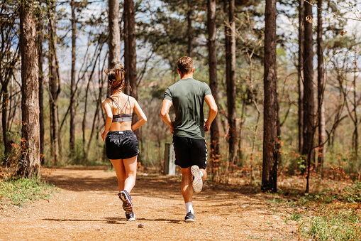 Man and woman exercising and jogging together at the park. Happy and smiling as they run along the path during sunset on a warm summer day