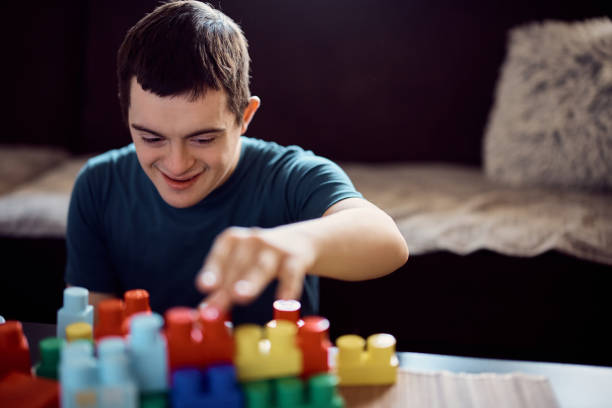 Young happy man with down syndrome stacking toy blocks at home.