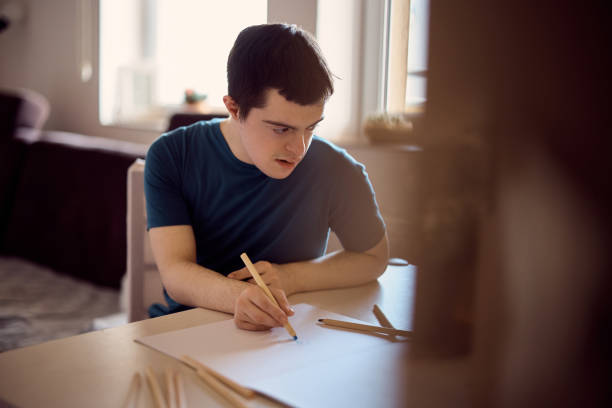istock Man with down syndrome drawing on the paper at home. 1387635322
