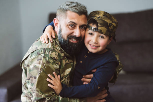 カメラを見つめながら抱き合う息子と軍人の父親 -軍帽をかぶった子供 -戦争の概念- - home interior arrival father family ストックフォトと画像