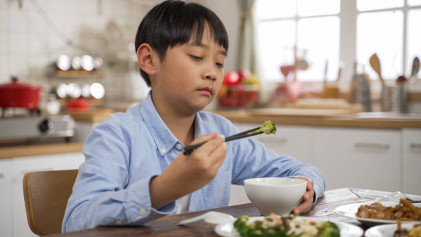 istock unhappy Asian Japanese little boy making a disgust expression while looking at green vegetable in bowl and shaking head show dislike and put it back at dining table 1387646451