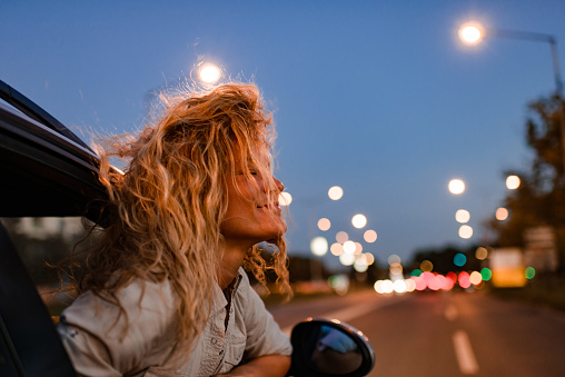 Young woman enjoying road trip while leaning on a car window.