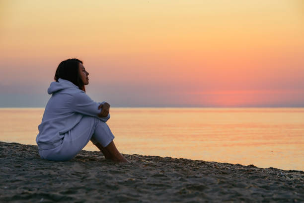 istock young woman sitting at sea beach looking on sunrise 1387647701