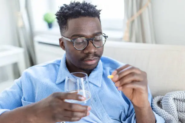 Photo of Black man hold pills and jar in his hands. Concept of healthcare and medicine, patient take daily dose of prescribed medicament, feel sick, antibiotics, painkillers or antidepressants. Close up