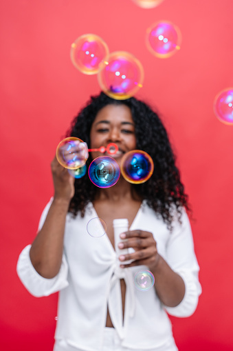 Vertical front view of african american woman playing funny with soap bubbles. Party background concept.