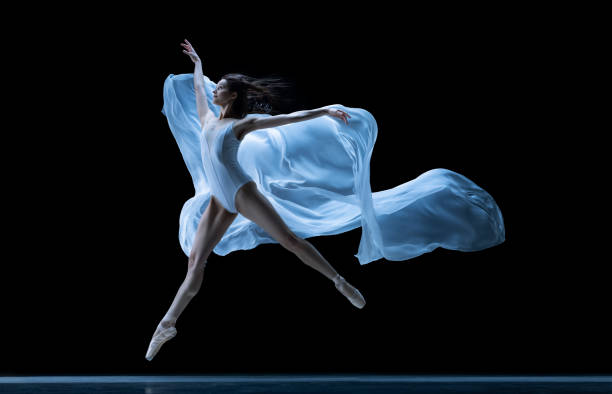 istock Graceful classic ballerina dancing with weightless fabric isolated on black studio background in neon. Theater, art, beauty, grace, action and motion concept. 1387651576
