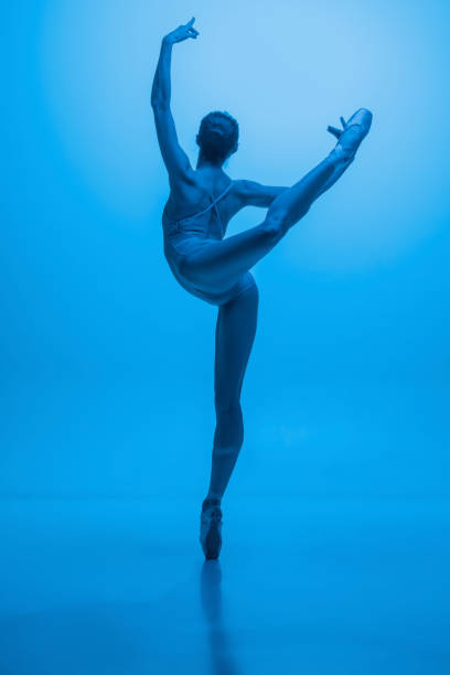 istock Back view of young and graceful ballet dancer isolated on blue studio background in neon light. Art, motion, action, flexibility, inspiration concept. 1387651615
