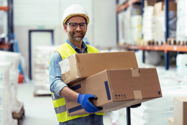 istock Handosme worker holding cardboard boxes while looking at camera in store warehouse 1387652091