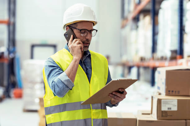 istock Mature worker talking with smartphone while passing list of material that has arrived at the store warehouse. 1387652187