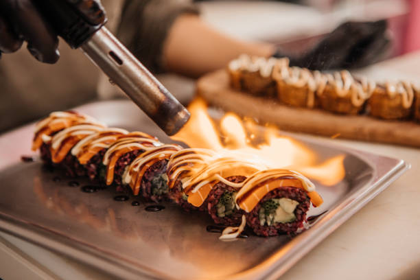 Vegan Sushi restaurant chef flaming a dish An expert female vegan sushi chef preparing tasty flaming food in a local restaurant sushi plate stock pictures, royalty-free photos & images