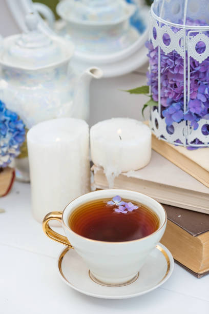 istock A visual for content. Still life in vintage style. A mug with a drink, an old book, a cage, candles and hydrangea flowers in the garden on a white wooden table. The concept of a tea ceremony. 1387664268