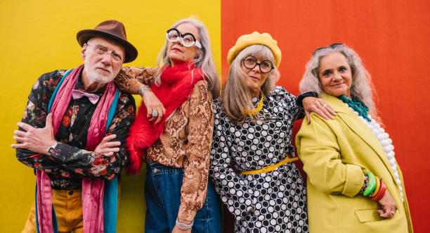 Active elderly people standing together against a colourful wall Active elderly people looking at the camera while standing together against a colourful wall. Group of four senior citizens feeling confident and youthful in colourful clothing. eccentric photos stock pictures, royalty-free photos & images