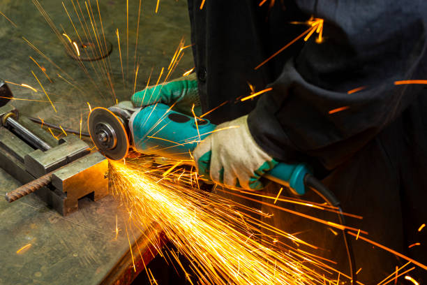 istock Metal Machining Concepts. Professional Fitter in Protective Gloves and Uniform Using Gringer Tool For Metal Work With Bunch of Sparks in Workshop. 1387670350