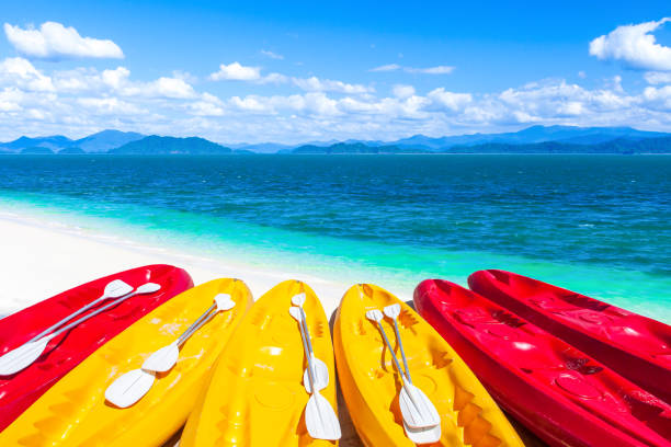 Colorful sea kayaks on a tropical sand beach on a summer day, an island, blue sea, white clouds in the blue sky in the background. Holidays, vacations concepts.