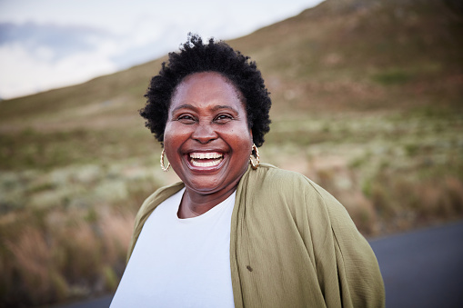 Portrait of a carefree mature African woman laughing while standing alone outside in the country in summer
