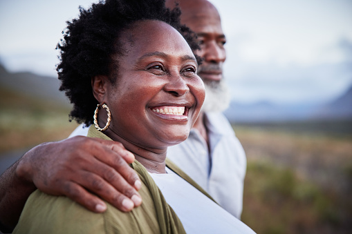 Mature African woman smiling while standing outdoors with her husband in the countryside in the late afternoon