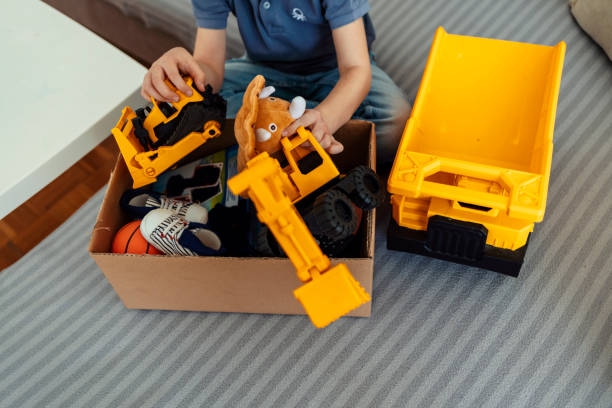Cropped shot of a satisfied young boy holding toy box in his hands labeled as donation box. Cheerful cute Caucasian boy holding full donation box with toys, sitting on couch at home during the day.