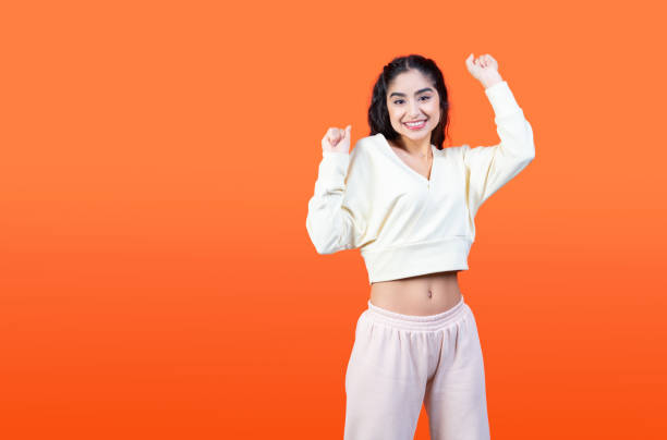 istock Beautiful brunette woman dancing on orange studio wall background with copy space. Template for a profitable commercial offer. 1387686582