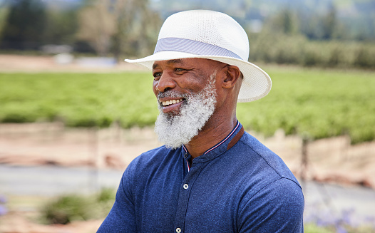 Stylish mature African man smiling while standing in front of a vineyard on a sunny day in the summertime