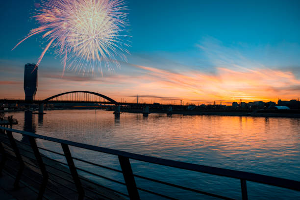 Celebration Holiday with fireworks on the scenic sky over the city river. Bridge at Blue hour sunset and skyscraper modern building silhouette on the Waterfront promenade. Copy space