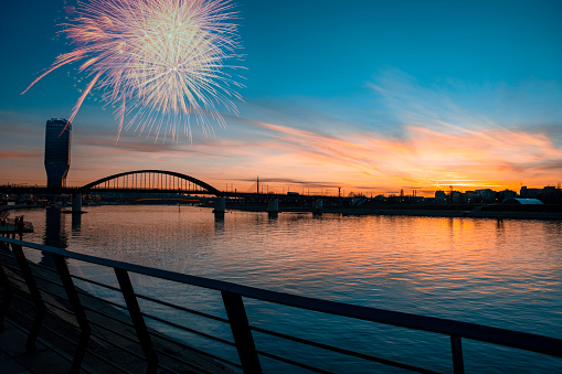 Celebration Holiday with fireworks on the scenic sky over the city river. Bridge at Blue hour sunset and skyscraper modern building silhouette on the Waterfront promenade. Copy space
