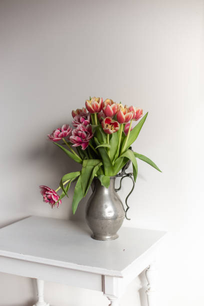 a bouquet of tulips in a vase on standing on a white furniture, spring vibes on the air