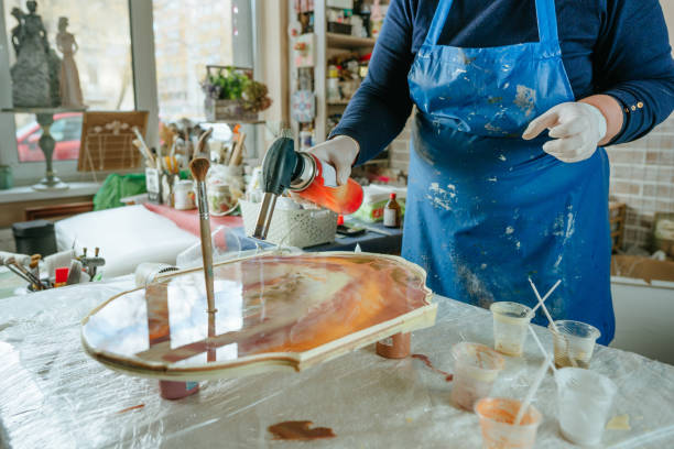 Female artist creating clock in resin art technique Artist creating clock board in resin art technique. Woman wearing rubber gloves using blowtorch for liquid resin with pigments. Selective focus. epoxy resin stock pictures, royalty-free photos & images