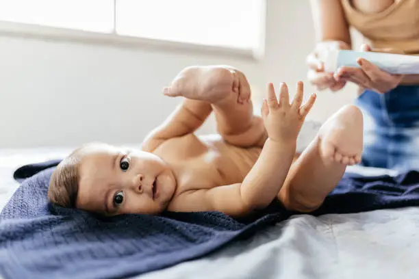 Photo of Mother changing baby's diaper in bed. Mother applies diaper rash cream.