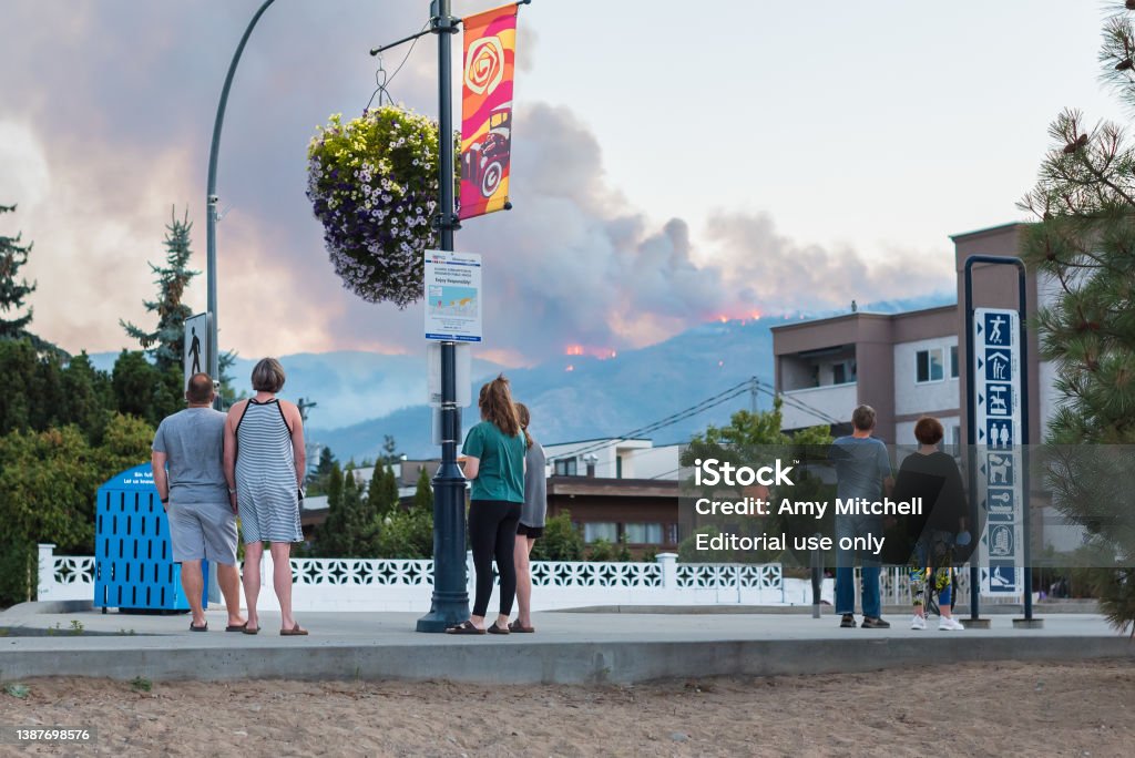 People watching forest fire in  hills above Penticton, BC, Canada Penticton, BC/Canada - August 29, 2021: Pedestrians watch from Lakeshore Drive as a forest fire flares up in the hills above the city. Forest Fire Stock Photo
