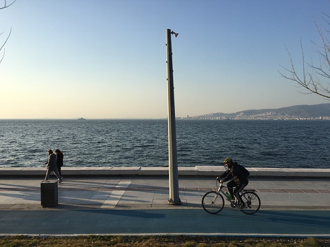 03/25/2022: People walking and cycling along the  Goztepe coastal walkway, road and tram line in a sunny weather.