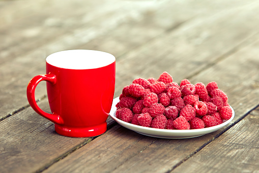 Fresh raspberries lie in a plate on the table on a summer day in the garden.