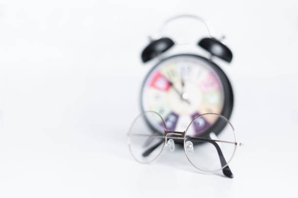 Black alarm clock on a white background. Glasses lie next to the clock. High quality photo