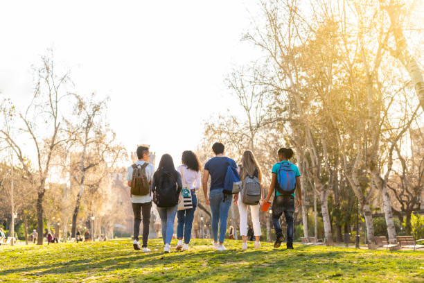 vista trasera de una fila de jóvenes estudiantes multiétnicos caminando juntos en el parque - campus fotografías e imágenes de stock
