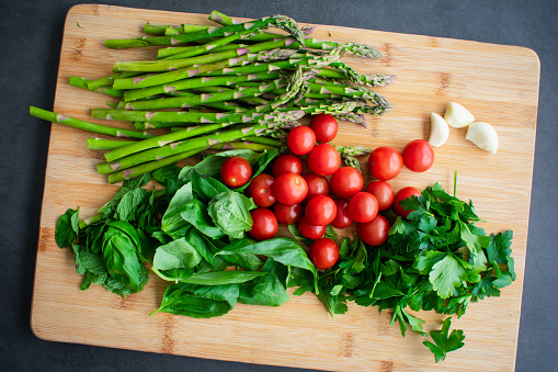 Cherry tomatoes, asparagus, basil, mint, parsley, and garlic cloves on a bamboo chopping board