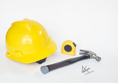 Yellow, construction hard hat with tools of tape measure, hammer and finishing nails isolated on white background.