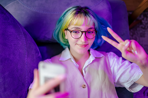 Beautiful teenage girl standing next to neon light  and taking selfie
