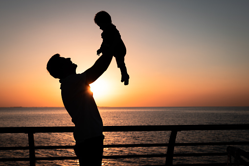 Man holding his baby boy by the seaside at sunset on a summer vacation silhouette. Father and son on the seaside spending time outdoors