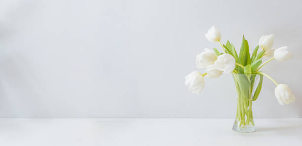 istock White spring tulips in a vase on a white table. Mock up for displaying works 1387713123