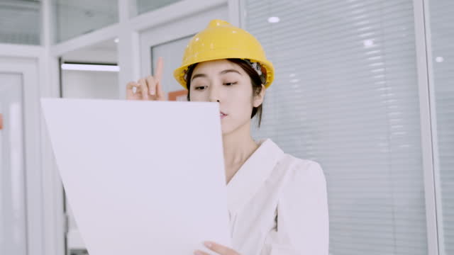 Beautiful young asian  female engineer in yellow helmet and check the design drawing