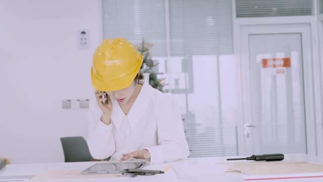 Beautiful young asian  female engineer in yellow helmet and using tablet design