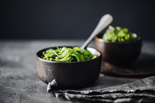 Close-up of a bowl of wakame with spoon on black table. Healthy and fresh green leafy vegetables on kitchen counter.