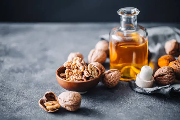 Close-up of vitamin E rich food on kitchen table. Bowl of walnuts and flax seed oil in glass bottle.