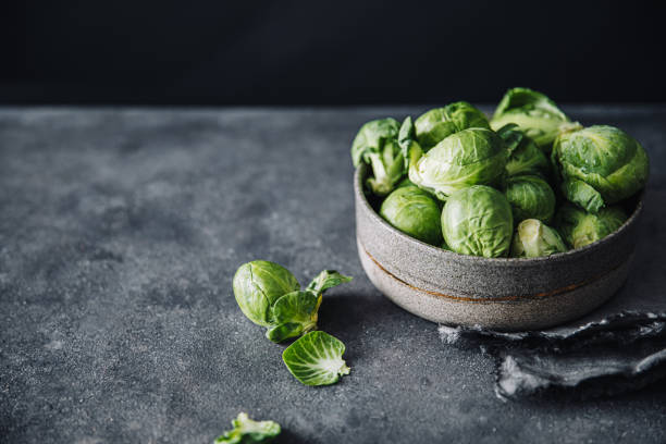 Close-up of raw brussels sprouts in a bowl on black table. Group of whole fresh green brussels sprouts on bowl with one fallen on table.