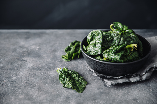Close-up of raw spinach in a bowl on black table. Fresh green spinach leaves on bowl with few fallen on a table.