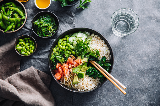 Table top view of a healthy salad bowl served on table. Chopped salmon fish, spinach, brussels sprouts, soybeans and chia seeds on a plate with chopsticks and glass of water.