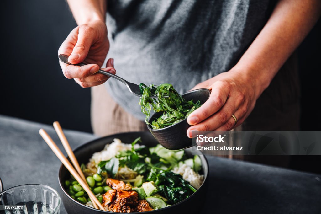 Close-up of woman eating omega 3 rich salad Close-up of woman eating omega 3 rich salad. Female having healthy salad consist of chopped salmon, spinach, brussels sprouts, avocado, soybeans, wakame and chia seeds in a bowl. Healthy Eating Stock Photo