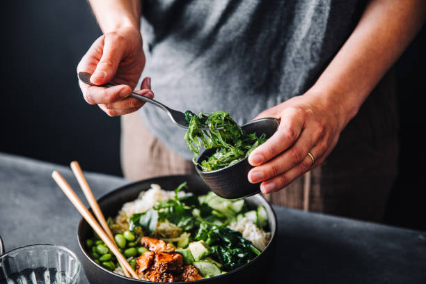 Close-up of woman eating omega 3 rich salad Close-up of woman eating omega 3 rich salad. Female having healthy salad consist of chopped salmon, spinach, brussels sprouts, avocado, soybeans, wakame and chia seeds in a bowl. chia seed photos stock pictures, royalty-free photos & images