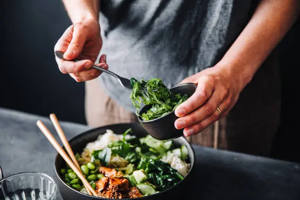 Close-up of woman eating omega 3 rich salad. Female having healthy salad consist of chopped salmon, spinach, brussels sprouts, avocado, soybeans, wakame and chia seeds in a bowl.