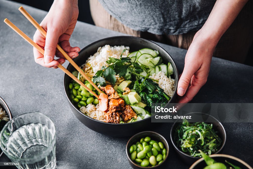Woman eating poke salad with chopsticks Close-up of a woman eating poke salad with chopsticks. Female hands using chopsticks for eating healthy salad. Protein Stock Photo