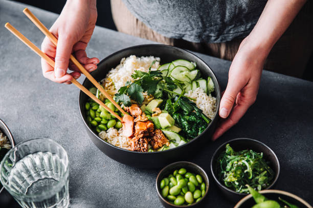 Woman eating poke salad with chopsticks Close-up of a woman eating poke salad with chopsticks. Female hands using chopsticks for eating healthy salad. eating chia seeds stock pictures, royalty-free photos & images